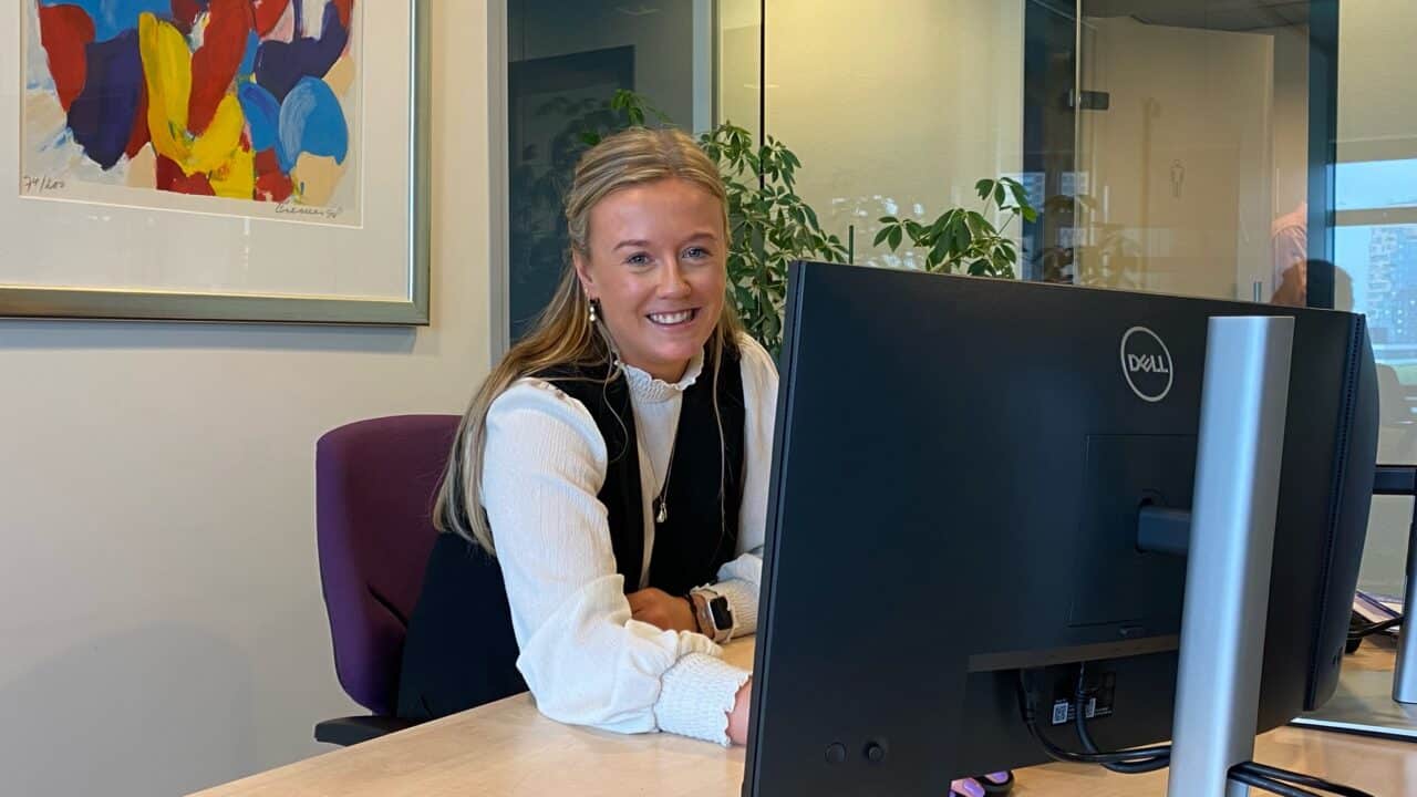 Vrouwlijke collega die lachend achter haar computer scherm zit.