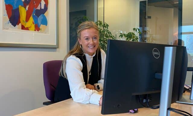 Vrouwlijke collega die lachend achter haar computer scherm zit.