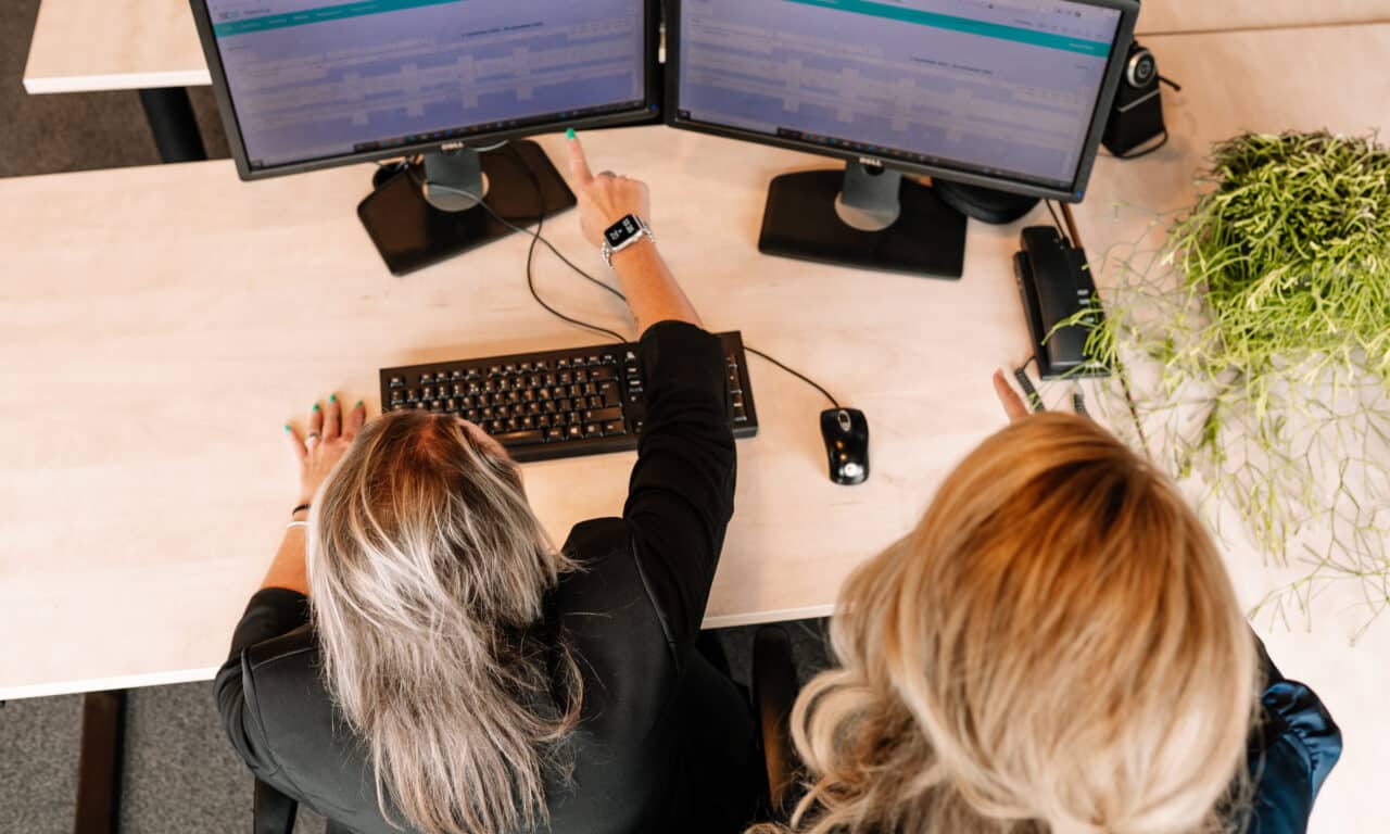 Een Financial Controller aan het overleggen met een collega achter computerschermen